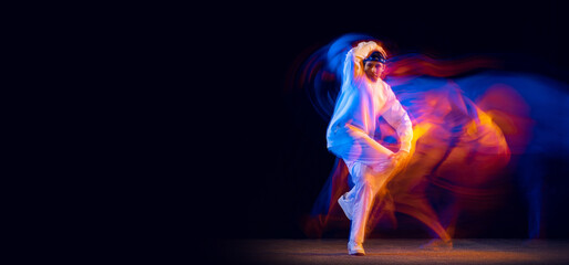 Stylish man in sports white suit dancing hip-hop isolated on dark background in mixed neon light. Youth culture, hip-hop, movement, style and fashion, action.