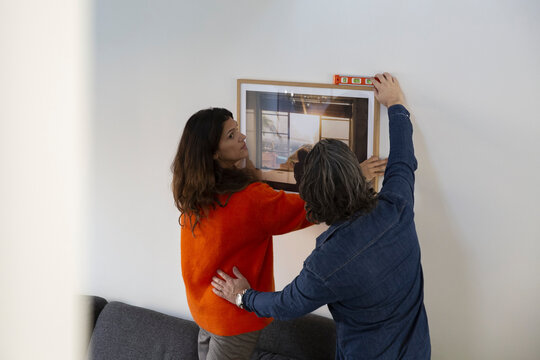 Heterosexual couple measuring level for hanging picture frame on wall while relocating in new house
