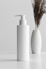 White cosmetic shampoo dispenser bottle mockup with a dry flower on the white table.
