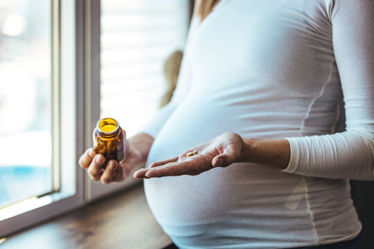 Close-up Of Pregnant Woman Hand With Glass Of Water And Vitamin Pill. Prenatal Vitamins And Supplements. Unrecognizable black pregnant woman taking pills capsules and glass of water