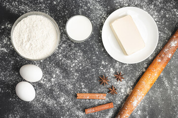Raw food ingredients for baking, flour, eggs, milk and butter on dark background, top view