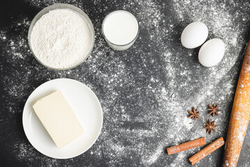 Raw food ingredients for baking, flour, eggs, milk and butter on dark background, top view