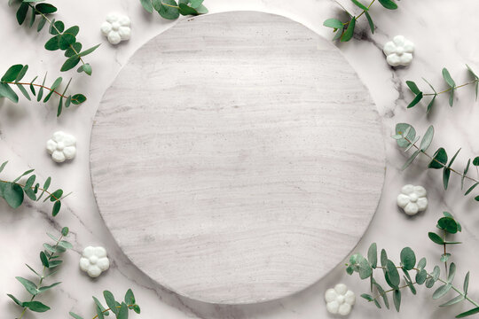 Wintertime mockup with copy-space on round, circle stone board. Fresh eucalyptus leaves and twigs. Top view on off white marble table. Winter flat lay background .