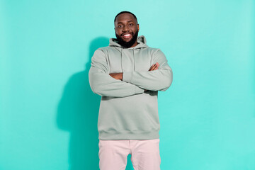 Portrait of attractive cheerful sportive guy folded arms wearing hood isolated over bright teal...