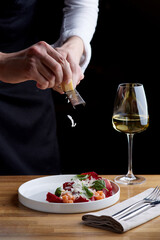 The chef prepares a salad with salmon. Rubs cheese on a grater. salmon salad with beet cheese and green leaves on wooden table with glass of white wine.