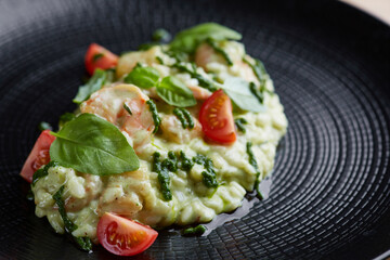 risotto with pesto, basil and cherry tomatoes closeup in black plate on wooden table. risotto on wooden table restaurant