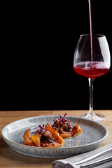 beef with sauce and sweet potato on a restaurant table with a glass of wine close up. restaurant dinner with dark background