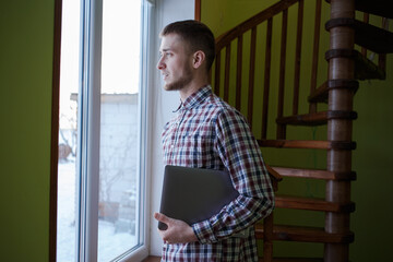 Guy in a plaid shirt with a laptop looks out the window