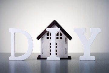 Home renovation construction diy concept. Word DIY with model of house on grey background.