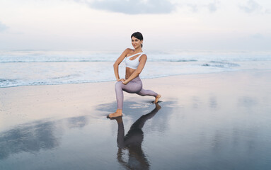 Portrait of young Caucaisan woman in sportive clothes looking at camera during morning stretching workout at coastline beach, attractive fit girl slimming while doing pilates and aerobic exercises