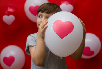 The boy with heart balloons congratulates with valentine's day, on a red background.