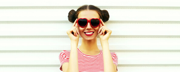 Portrait of cheerful smiling young woman wearing a red heart shaped sunglasses striped t-shirt with cool hairstyle on white background