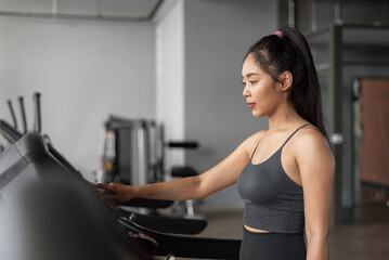 Fototapeta na wymiar Asian woman exercises in fitness. Young healthy woman in sportswear is running on a treadmill in gym.
