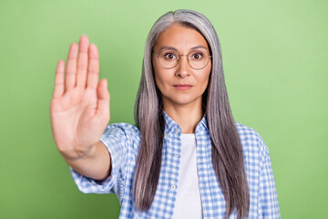 Photo of strict aged grey hairdo lady show stop wear spectacles plaid shirt isolated on green color...