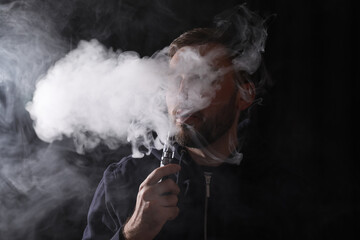 Man using electronic cigarette on black background