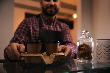 Barista putting takeaway coffee cups with cardboard holder on glass table in cafe, closeup