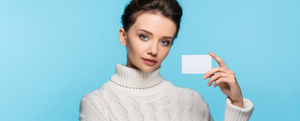 Brunette model in knitted sweater holding blank card isolated on blue, banner.