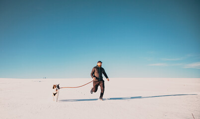 man and his happy white dog enjoying winter snow outdoors on sunny day