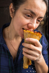 A pretty middle-aged woman in a purple plaid shirt is eating a pizza cone. Fast food.