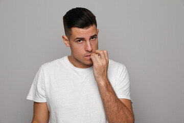 Man biting his nails on grey background. Bad habit