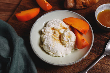 Homemade ricotta cheese or cheese curd served with fresh persimmon and honey and croissante on wooden background. Healthy breakfast. Haze effect. Selective focus