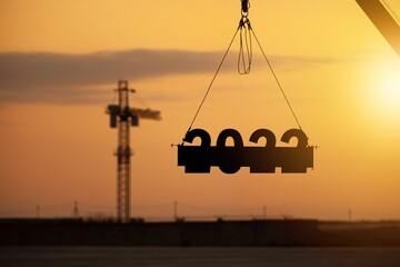 Silhouette of a construction crane at a construction site raising the number 2022 year. Concept for New Year for development and business