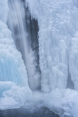 Winter landscape of a cascade captured with motion blur and framed by blue ice, Comstock Creek, Michigan, USA