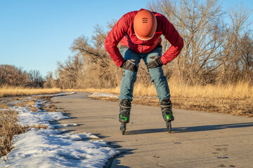 tired male skater is taking a break, inline skating on a paved bike trail along Poudre River in...