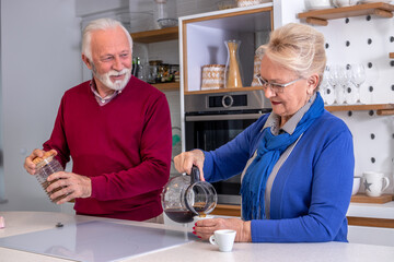Happy senior couple preparing their morning coffee in the kitchen, smiling and talking to each other.