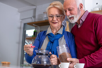 Happy senior couple preparing their morning coffee in the kitchen, smiling and in love with each other.