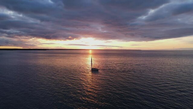 Aerial SILHOUETTE view of a lonely sailboat at open sea with an America Sail with Sunset behind cumulus clouds and the sun reflecting on the ocean, Marthas Vineyard, Massachussetts