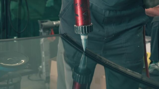 Process of preparing windshield for replacement in car service. Worker applies special adhesive sealant to windscreen before installation on auto.