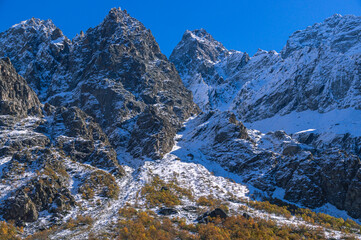 Snow in autumn in the mountains.White snow and yellowed trees in autumn in the mountains on a clear day. The Caucasus Mountains in North Ossetia. Landscape in the mountains and blue sky with clouds