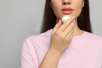 Young woman applying lip balm on grey background, closeup. Space for text - obrazy, fototapety, plakaty