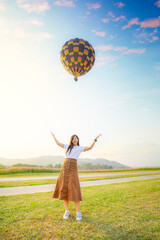 A woman standing on the green grass and happily take a picture with a hot air balloon 