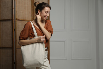 Happy young woman with blank eco friendly bag indoors. Space for text