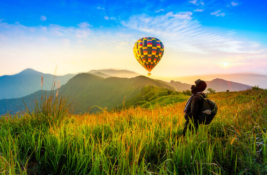 Photographer travels with a camera to capture the sunrise while standing on top of a hill and having a balloon.