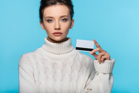 Young woman in knitted sweater holding credit card isolated on blue.