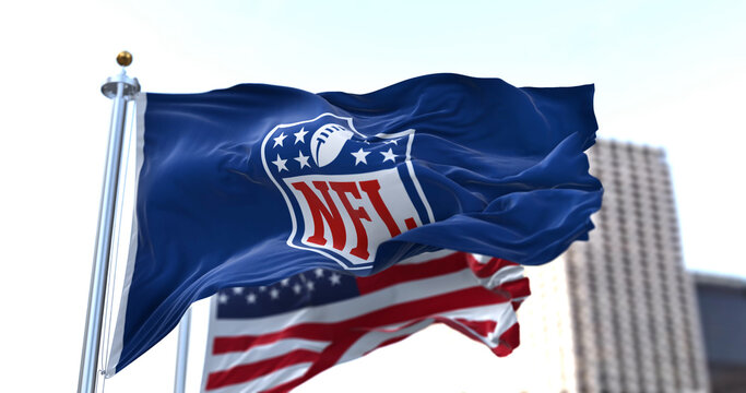 The flag with the NFL logo waving in the wind with the US flag blurred in the background