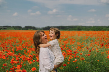 Fototapeta premium Happy Mother's Day. Little boy and mother is playing in a beautiful field of red poppies. People and nature. Rural scene