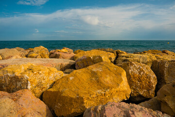 Fototapeta na wymiar Big stones of breakwater by the sea, blue sky clouds