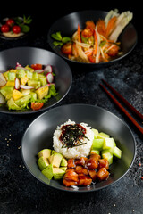 Poke with salmon and avocado, salad with avocado and vegetables, Chinese cuisine on dark stone table