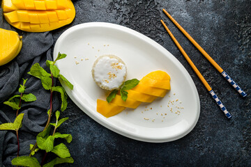 Mango with boiled rice on white plate on dark stone table, Chinese cuisine top view