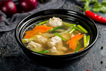Chicken soup with chicken meatballs and vegetables on black bowl, Chinese cuisine macro close up