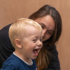 Mom looks and smiles at the son of a 3-year-old blond boy laughing out loud. Funny family