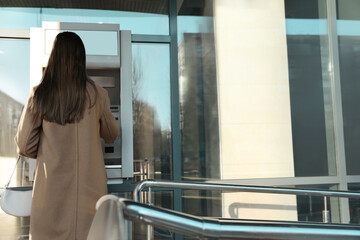 Young woman using cash machine for money withdrawal outdoors, back view