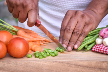 Close up of man's hands while chopping fresh vegetables on cutting board,