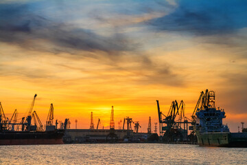 Fototapeta na wymiar Silhouettes of harbor cranes and cargo ships in sea port on the background of sunset, Varna, on the Black Sea coast of Bulgaria