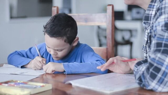 boy child doing homework learning at home with mother sitting at a table stock video
