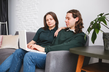 Obraz premium Couple sitting on the sofa with notebook and phone. Man and woman communicating on the electronic gadgets. Social isolation, distant learning students